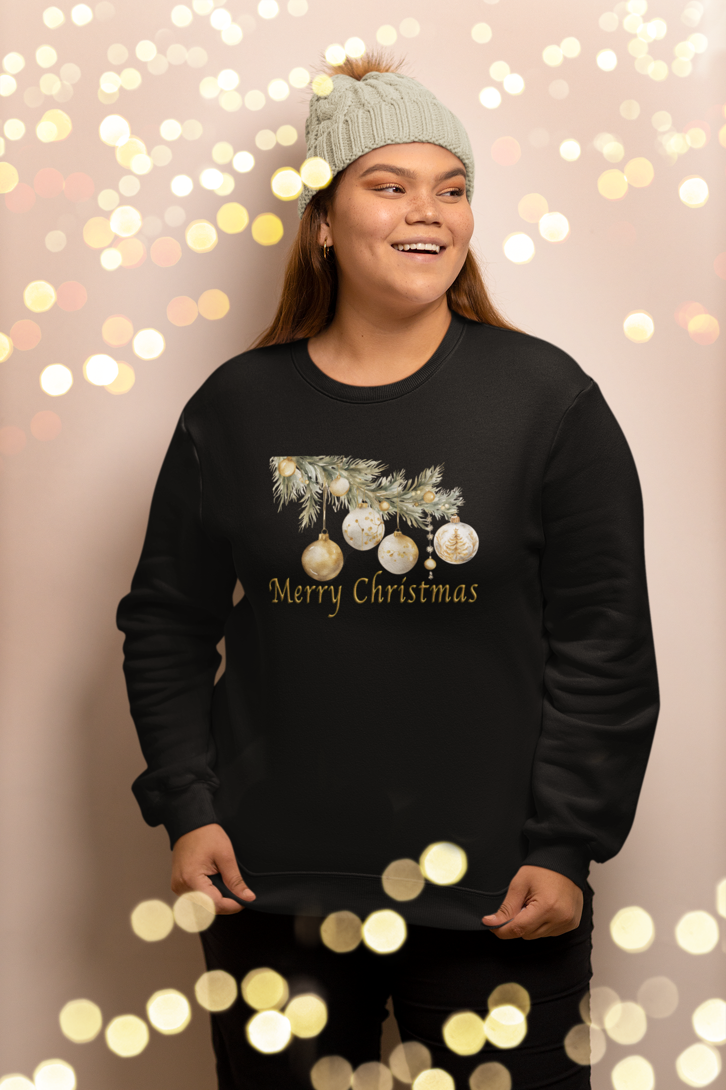Person wearing a black 'Merry Christmas' sweater with a tree and ornaments design, standing against a festive light background.
