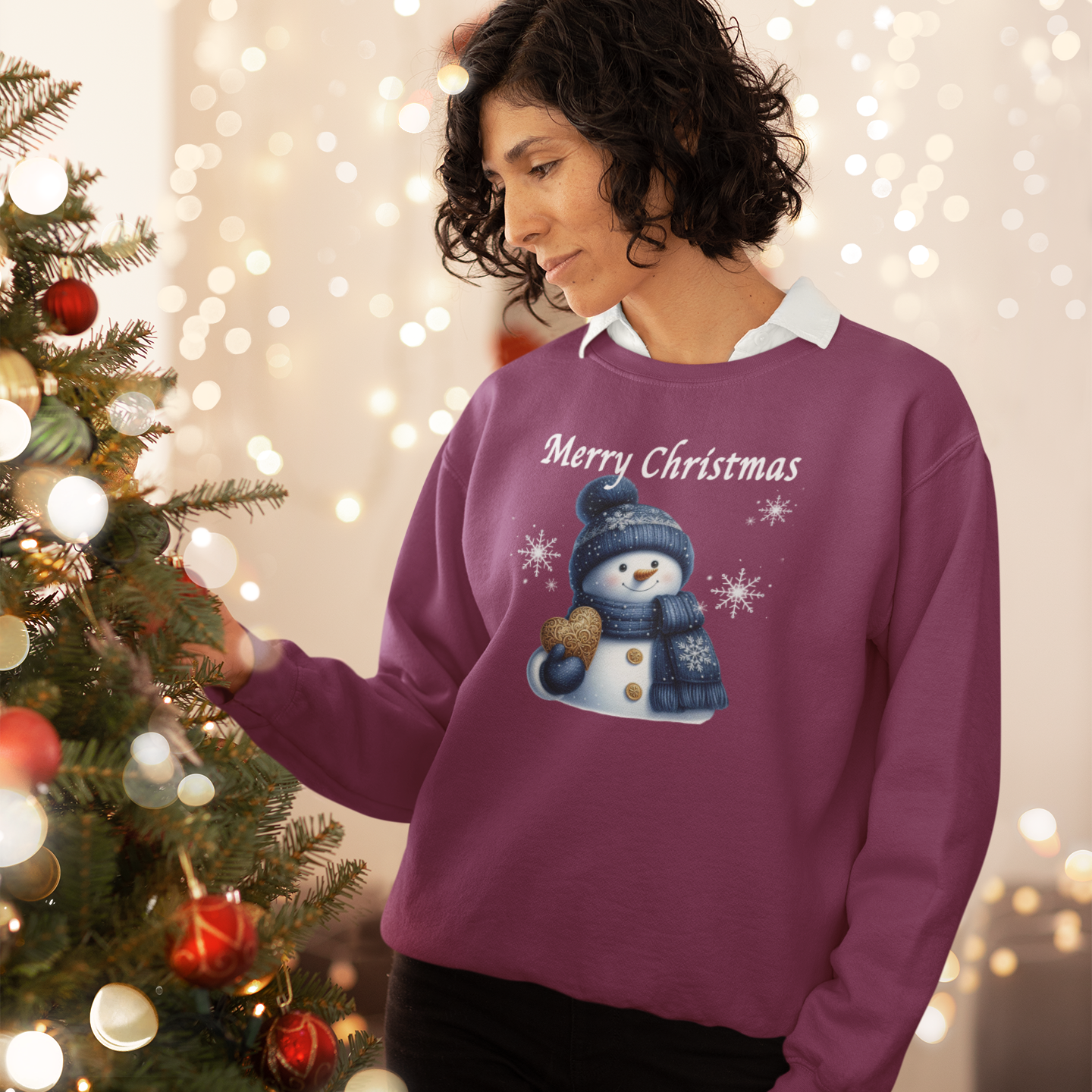 Person wearing a purple 'Merry Christmas' sweater with a snowman design, standing next to a decorated Christmas tree.