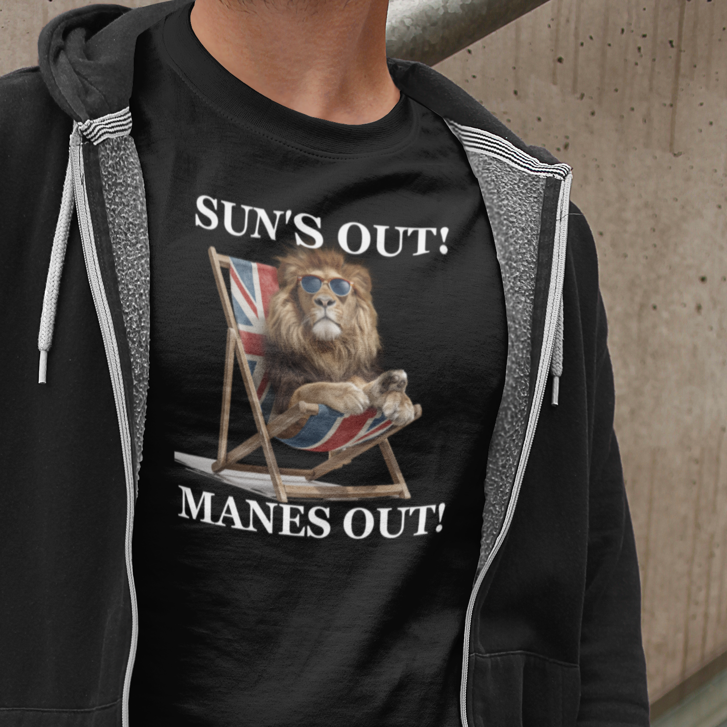 Person wearing a black t-shirt with a graphic design and text, standing against a concrete wall.