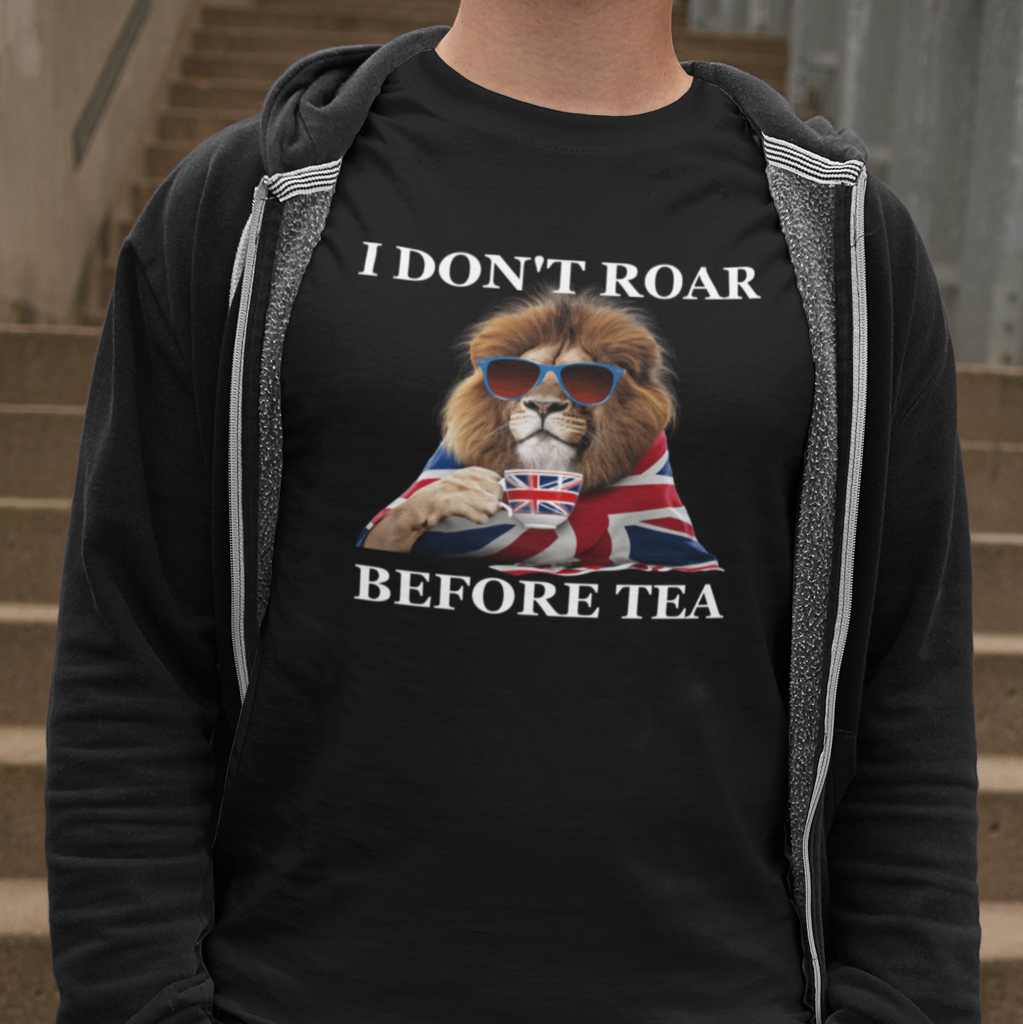 Person wearing a black hoodie with a lion graphic and text 'I Don't Roar Before Tea' on a staircase.