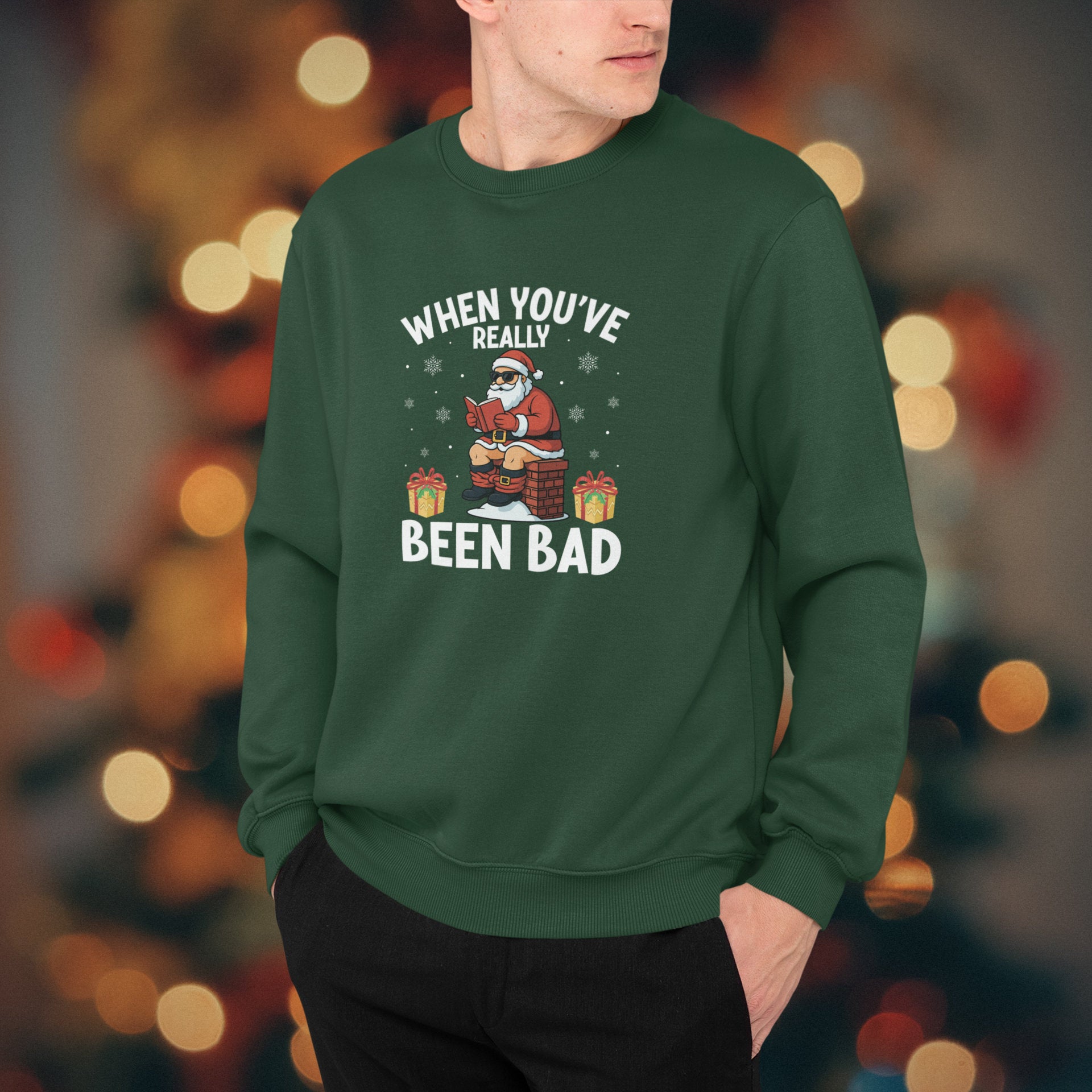 Person wearing a green sweatshirt with a Christmas design and text, against a blurred festive background.