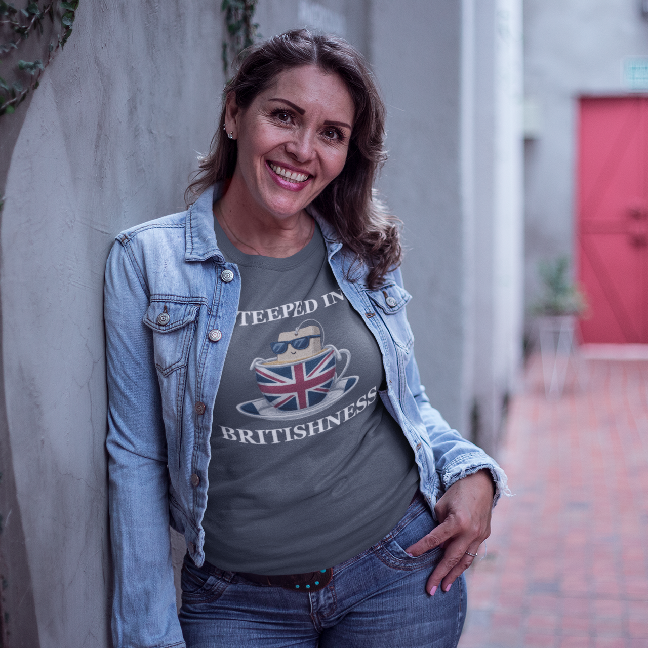 Woman wearing a gray t-shirt with a design and text, standing in an outdoor setting with a red door in the background.