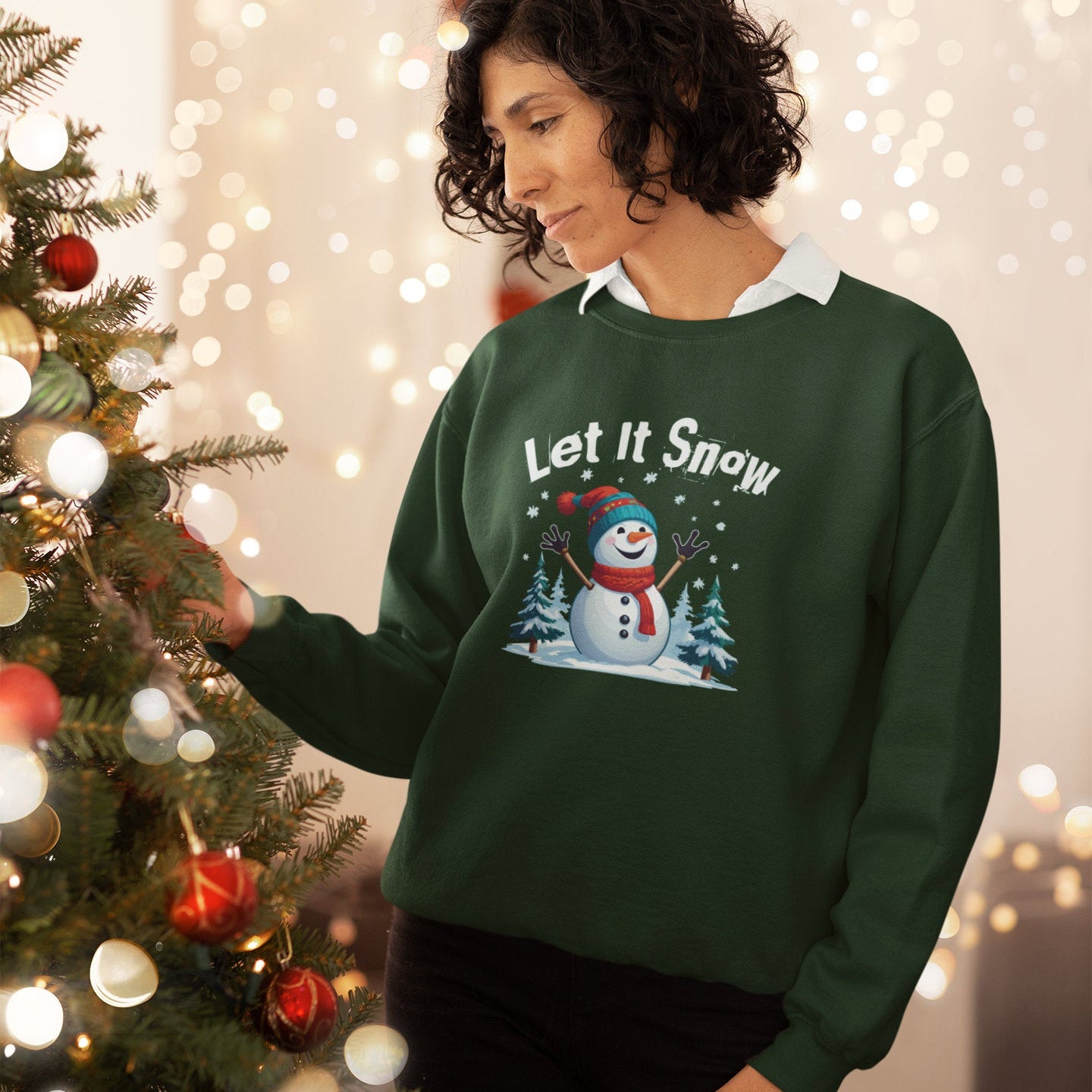 Person wearing a green 'Let It Snow' sweater with a snowman graphic, standing next to a decorated Christmas tree.