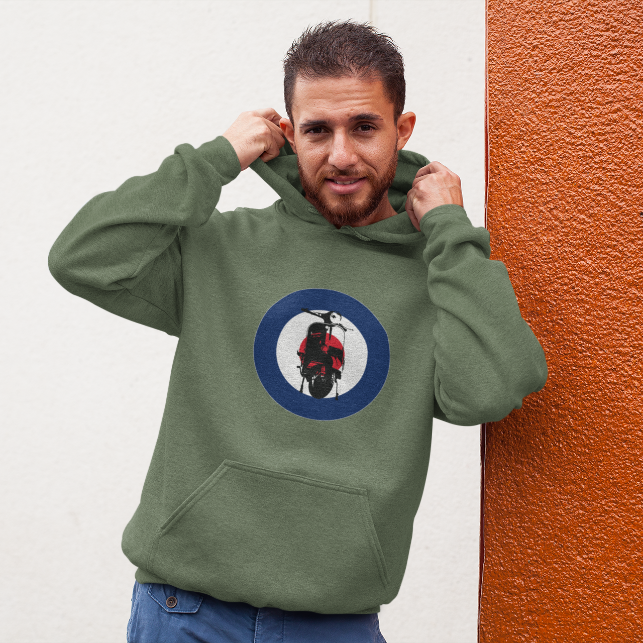 Man wearing a green hoodie with a circular logo against a white and orange wall.