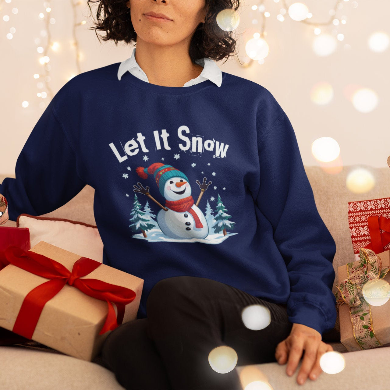 Person wearing a navy blue sweater with a snowman design and 'Let It Snow' text, surrounded by Christmas presents and lights.