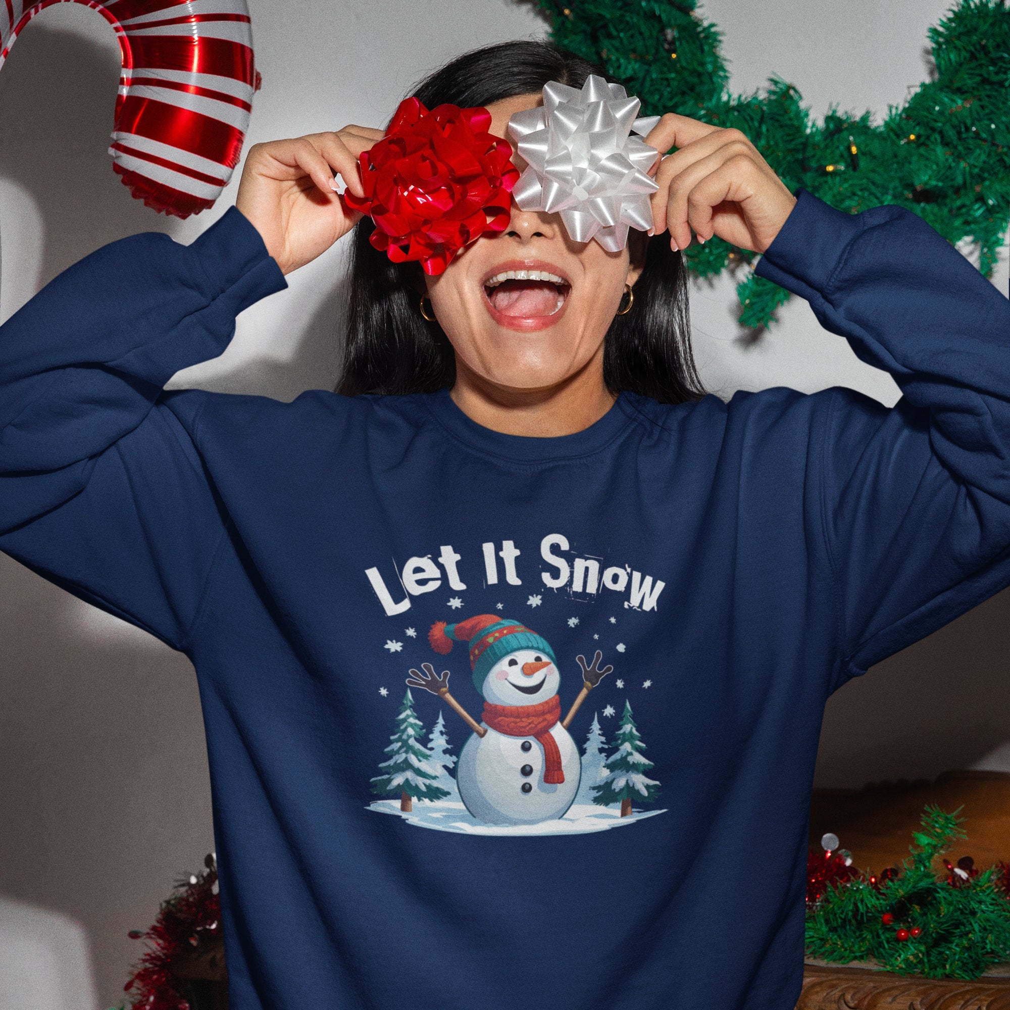 Person wearing a navy blue sweatshirt with a snowman graphic and 'Let It Snow' text, holding festive balloons.