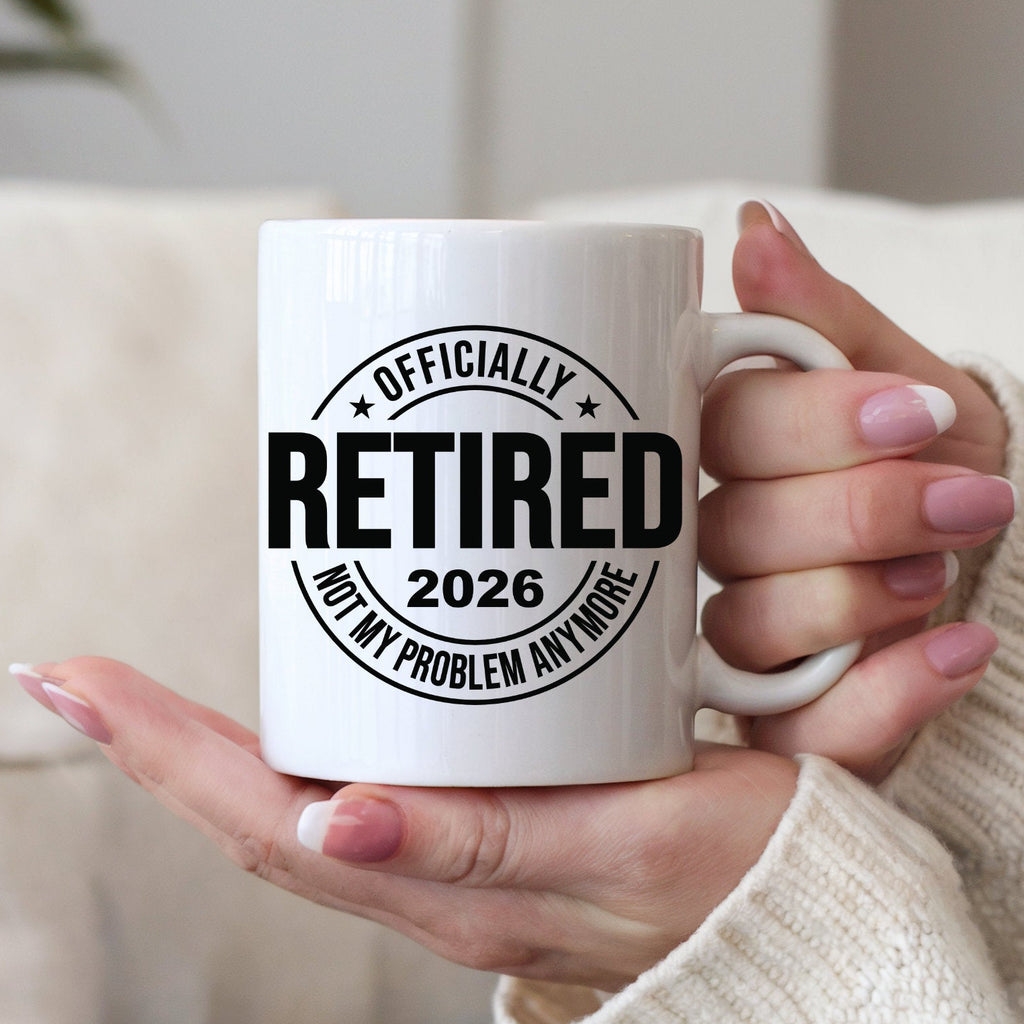 Person holding a white mug with 'Officially Retired 2026 Not My Problem Anymore' text.
