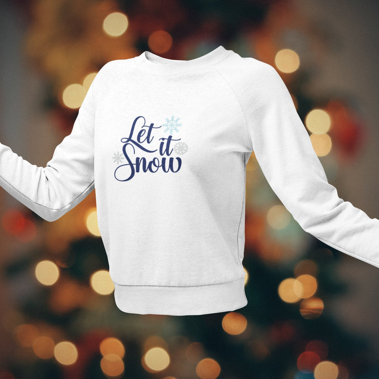 White sweatshirt with 'Let it Snow' text on a blurred Christmas tree background