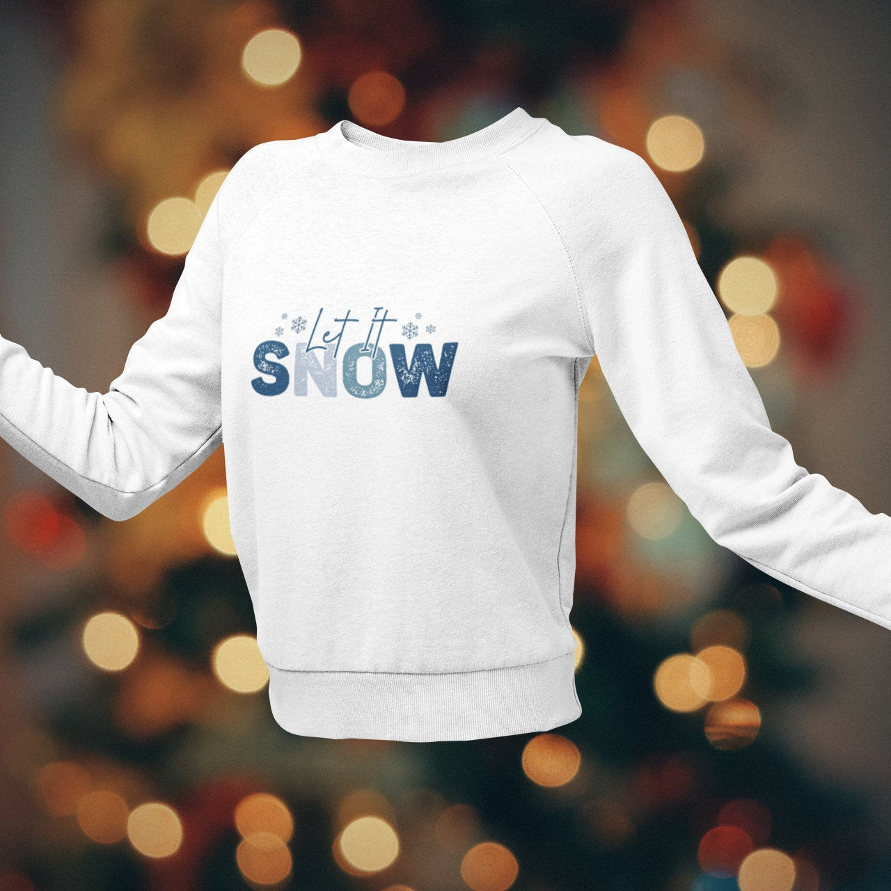 White sweatshirt with 'Let it Snow' text on a blurred Christmas tree background