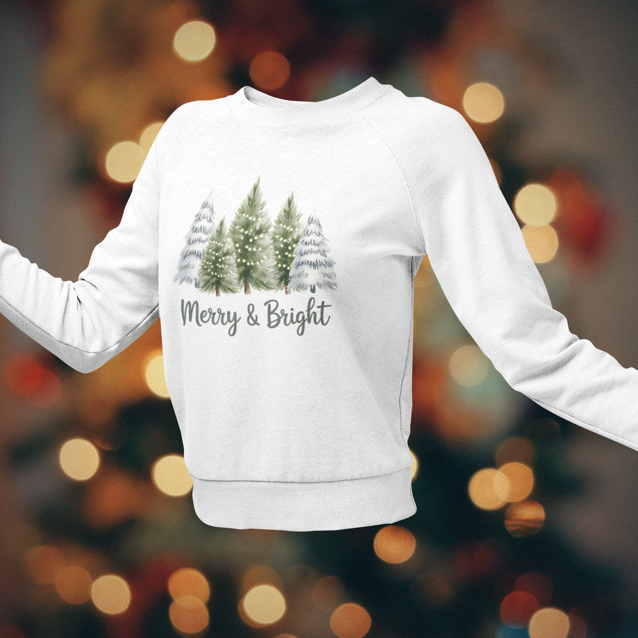 White sweatshirt with Christmas tree design and 'Merry & Bright' text against a blurred festive background
