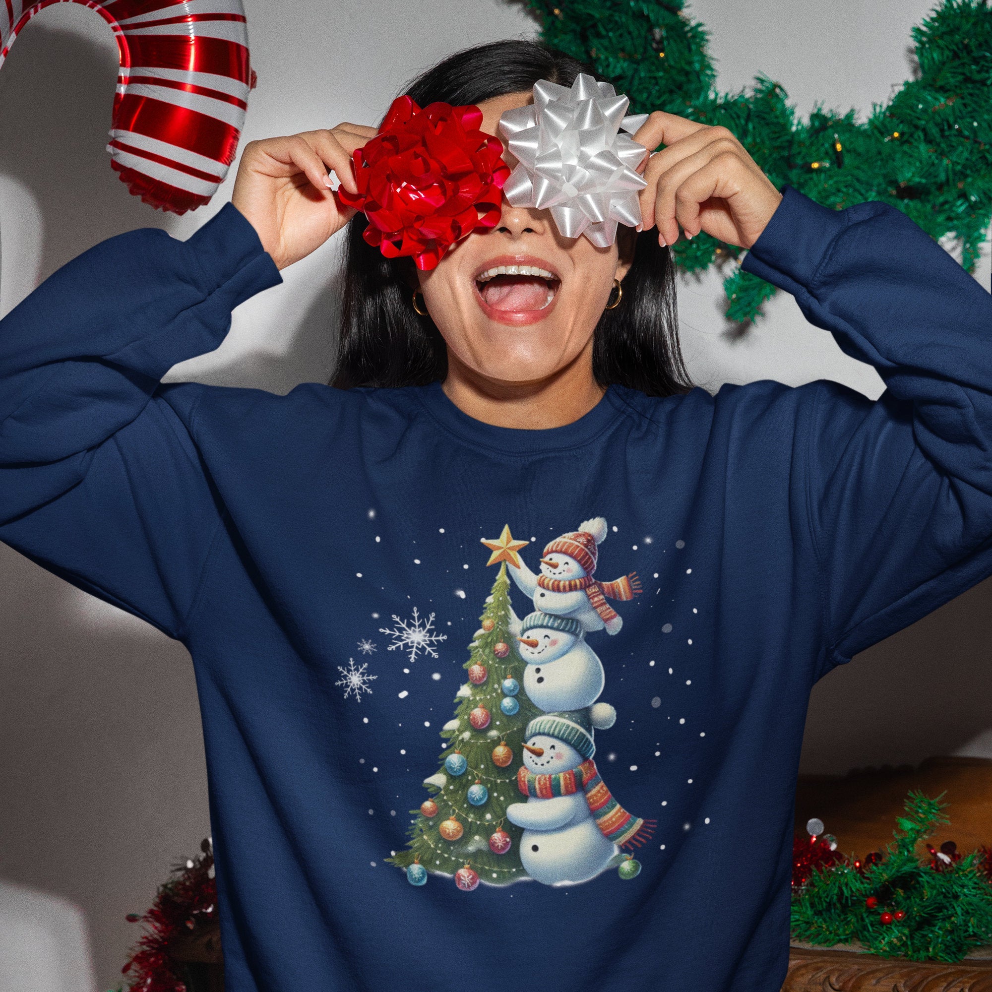 Person wearing a blue Christmas-themed sweatshirt with snowmen and a tree, holding festive balloons.