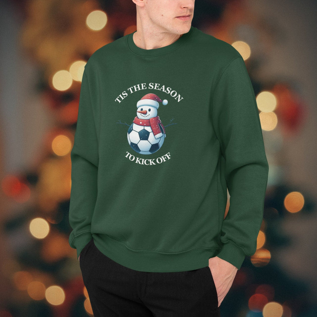 Person wearing a green sweatshirt with a snowman and soccer ball design, standing against a blurred festive background.