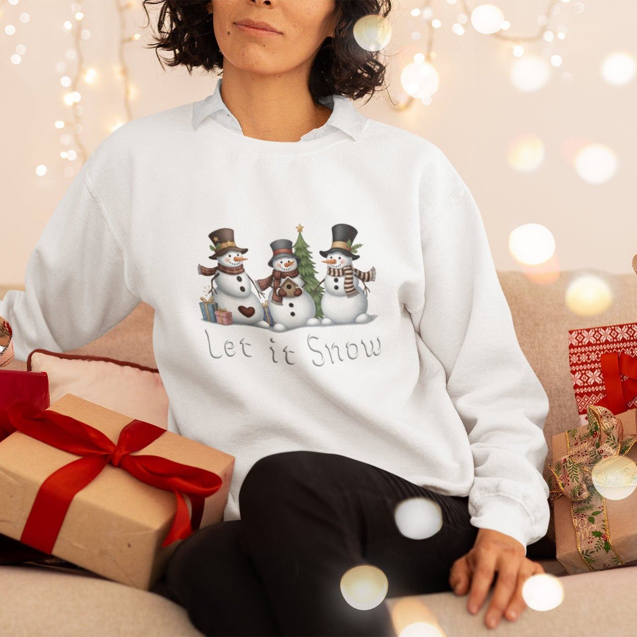 Person wearing a white sweatshirt with snowman design and 'Let it Snow' text, surrounded by Christmas presents and lights.