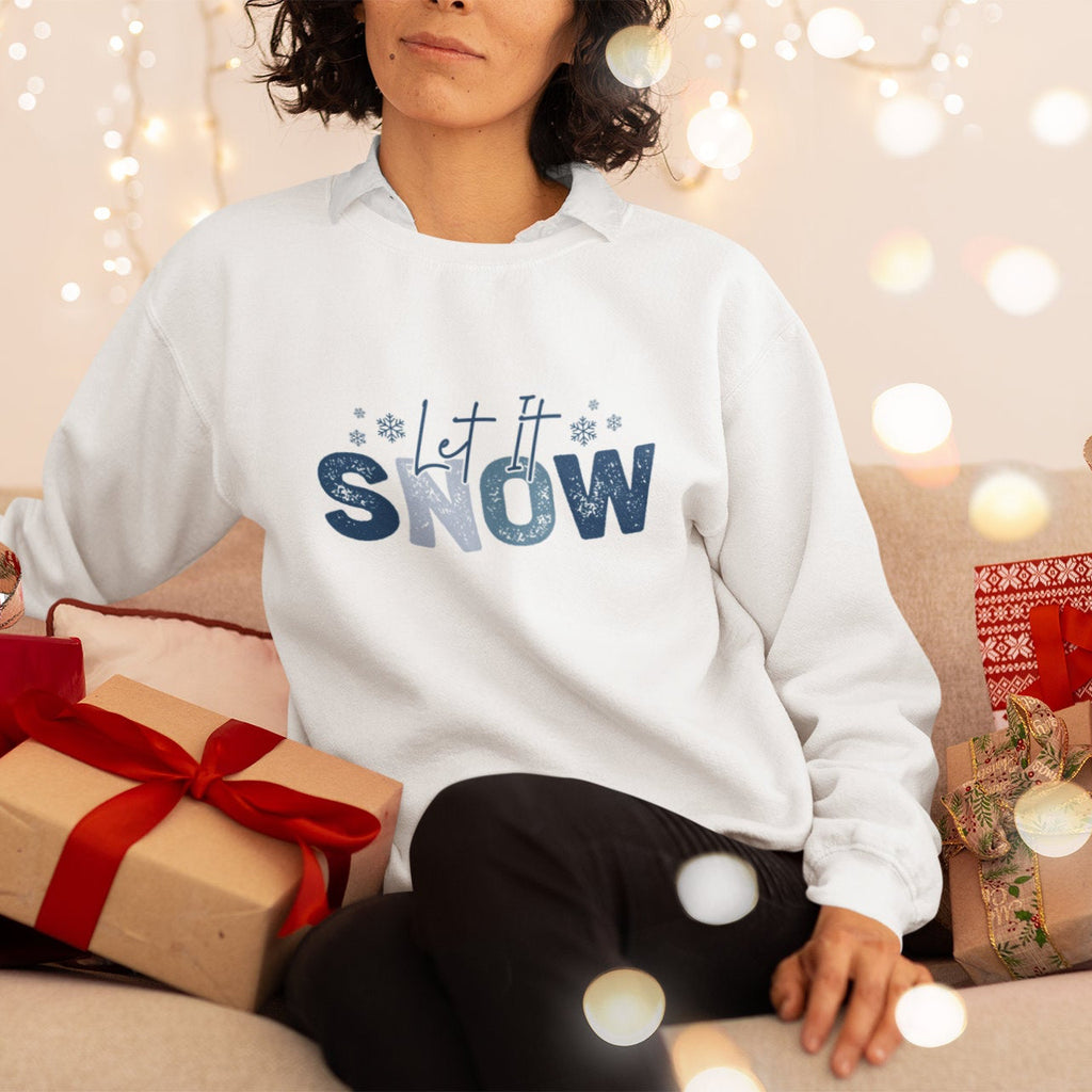 Person wearing a 'Let it Snow' sweater surrounded by Christmas presents and lights.