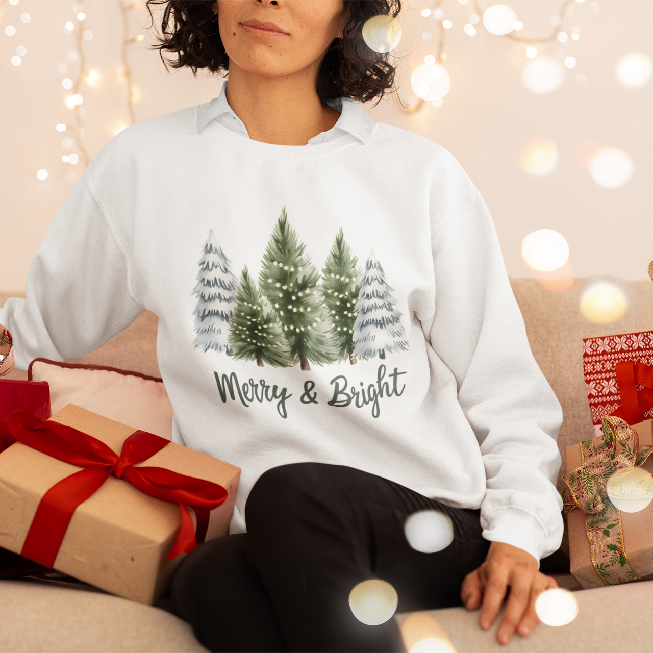 Person wearing a white sweatshirt with Christmas tree design and text, surrounded by festive decorations and presents.