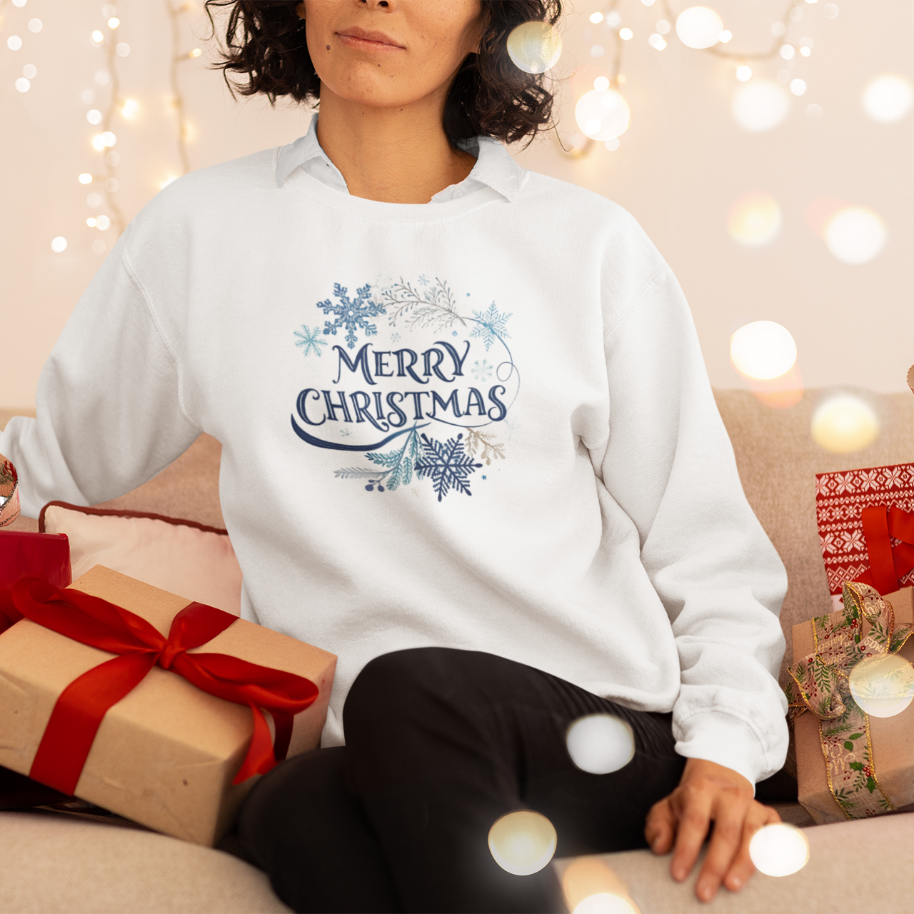 Person wearing a white sweatshirt with 'Merry Christmas' text, surrounded by festive presents and lights.